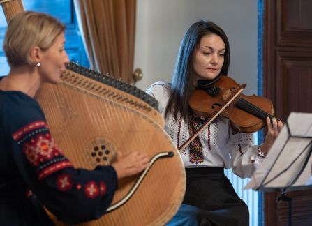 Fotografia. Dwie kobiety grają na instrumentach, na skrzypcach i bandurze.