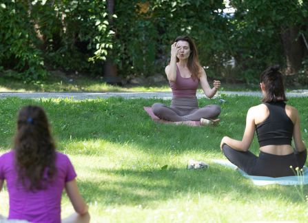 Fotografia. Lekcja jogi na zewnątrz. Kobiety siedzą po turecku na trawie.