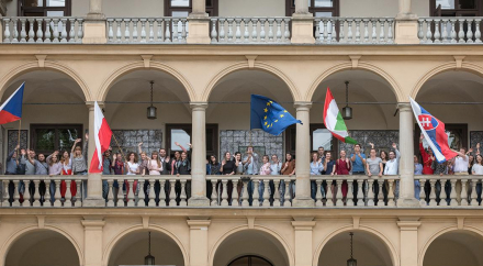 Fotografia grupy ludzi na loggii Willi Decjusza z różnorodnymi flagami