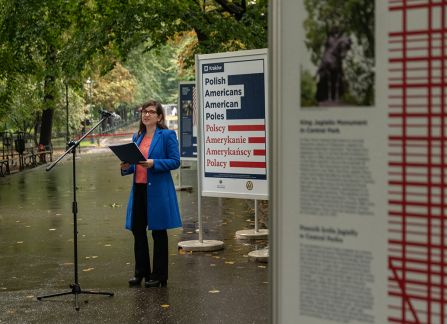 A photograph. An opening of the outdoor exhibition titled Polish Americans, American poles at planty in Krakow. Amy Steimann, Consul for Press and Culture gives a speech next to the row of posters.