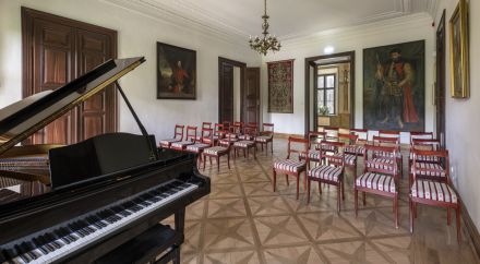 zdjęcie fortepianu, krzesł widowni i obrazów w jednej z sal w Willi Decjusza