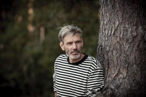 zdjęcie portretowe mężczyzny w średnim wieku w koszulce w paski, opartym o pień drzewa