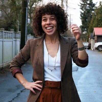 portrait picture of UNESCO resident Sarah Herman. The woman stands and smiles. A suburban landscapr in the background.