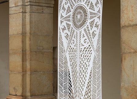 fotografia. wielkoformatowa wycinanka z tradycyjnym wzorem, eksponowana pomiędzy kolumnami arkad na fasadzie willi decjusza.