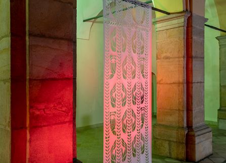 fotografia. wielkoformatowa wycinanka z tradycyjnym wzorem, eksponowana pomiędzy kolumnami arkad na fasadzie willi decjusza. Zdjęcie wykonane po zmroku, ekspozycja podświetlona na zielono i czerwono.